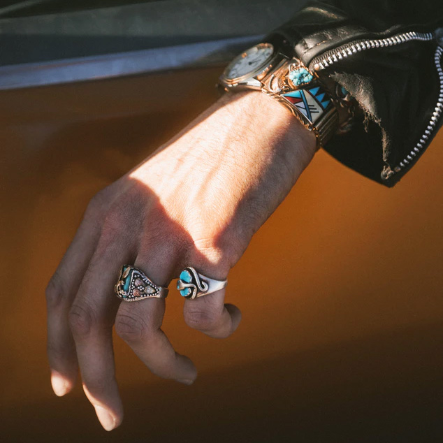 Homme portant des bijoux dont une montre en métal turquoise et des bagues en argent avec des pierres truquoise.. 